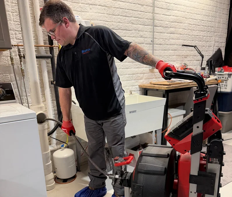 Rozga Plumbing Corp technician using drain cleaning equipment in a residential basement