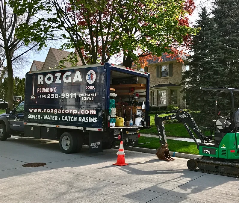 Rozga Plumbing Corp service truck and mini excavator on-site for sewer and water line repair in Southeastern Wisconsin