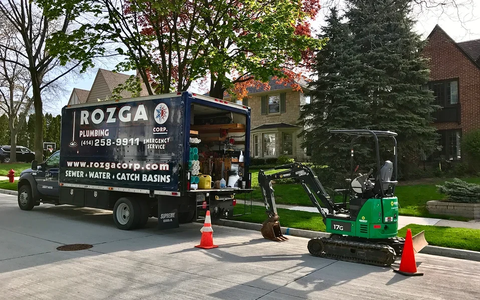 Rozga Plumbing Corp service truck and mini excavator on-site for sewer and water line repair in Southeastern Wisconsin