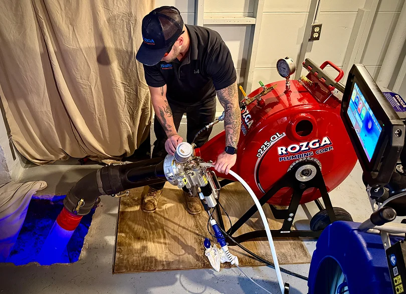 Rozga Plumbing Corp technician operating trenchless sewer lining equipment at a residential access point